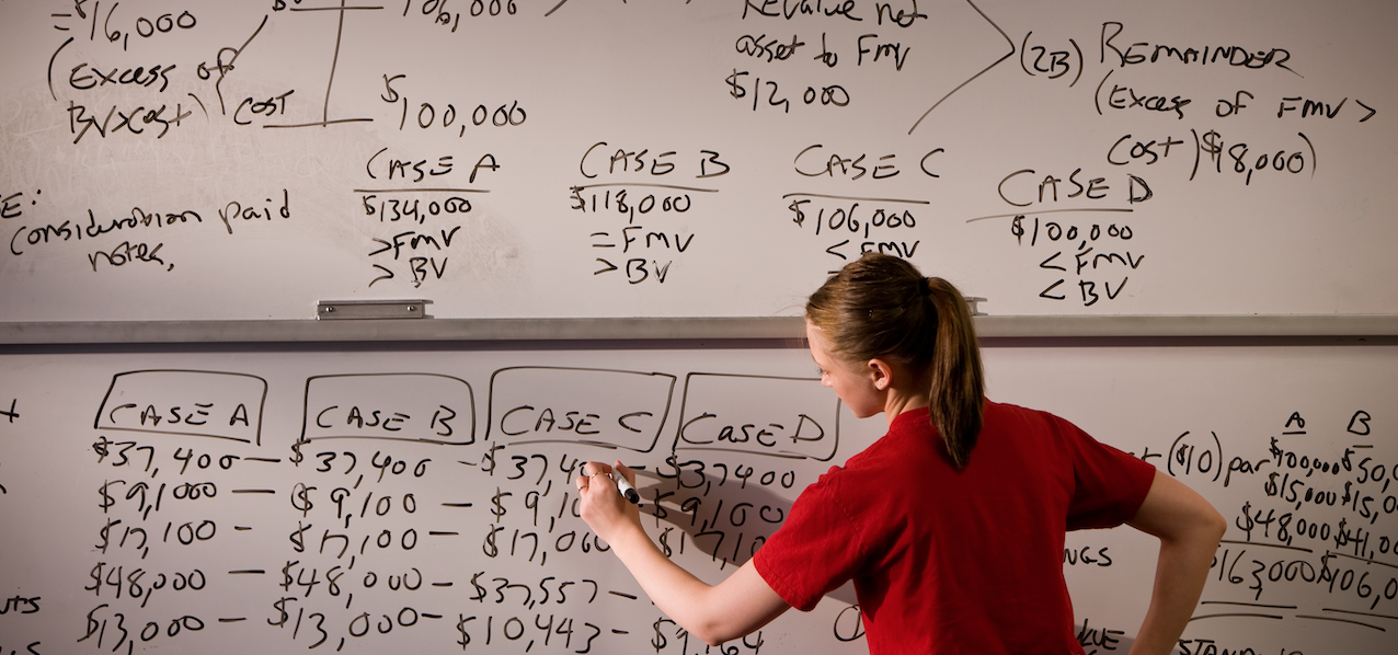 A woman working on accounting problems on a white board