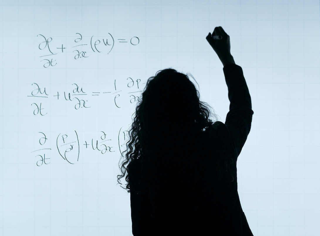 a person backlit against a white board, writing an equation. from pexels
